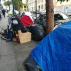 A homeless person sits under a blanket next to a cluster of tents in the Tenderloin May 13. Noah Arroyo / San Francisco Public Press