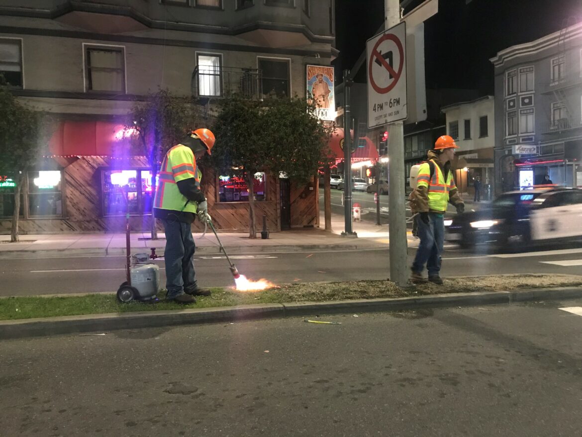 San Francisco city workers use blowtorches to remove grass and weeds from a median on Broadway at Polk Street on Feb. 3, 2020. City workers rely much less on herbicides than they did just five years ago, as health concerns mount.