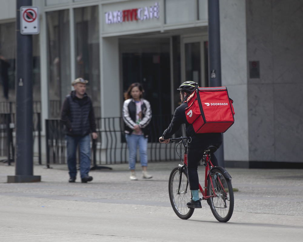 In this photo, a DoorDash delivery person rides a bicycle to make a deliver. Albertsons, Safeway’s parent company, plans to cut hundreds of grocery delivery positions in California and replace them with gig workers from DoorDash.