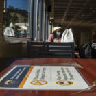 An Alcatraz employee is seated on a ferry to the island with a sign instructing COVID-19 protocol in the foreground.