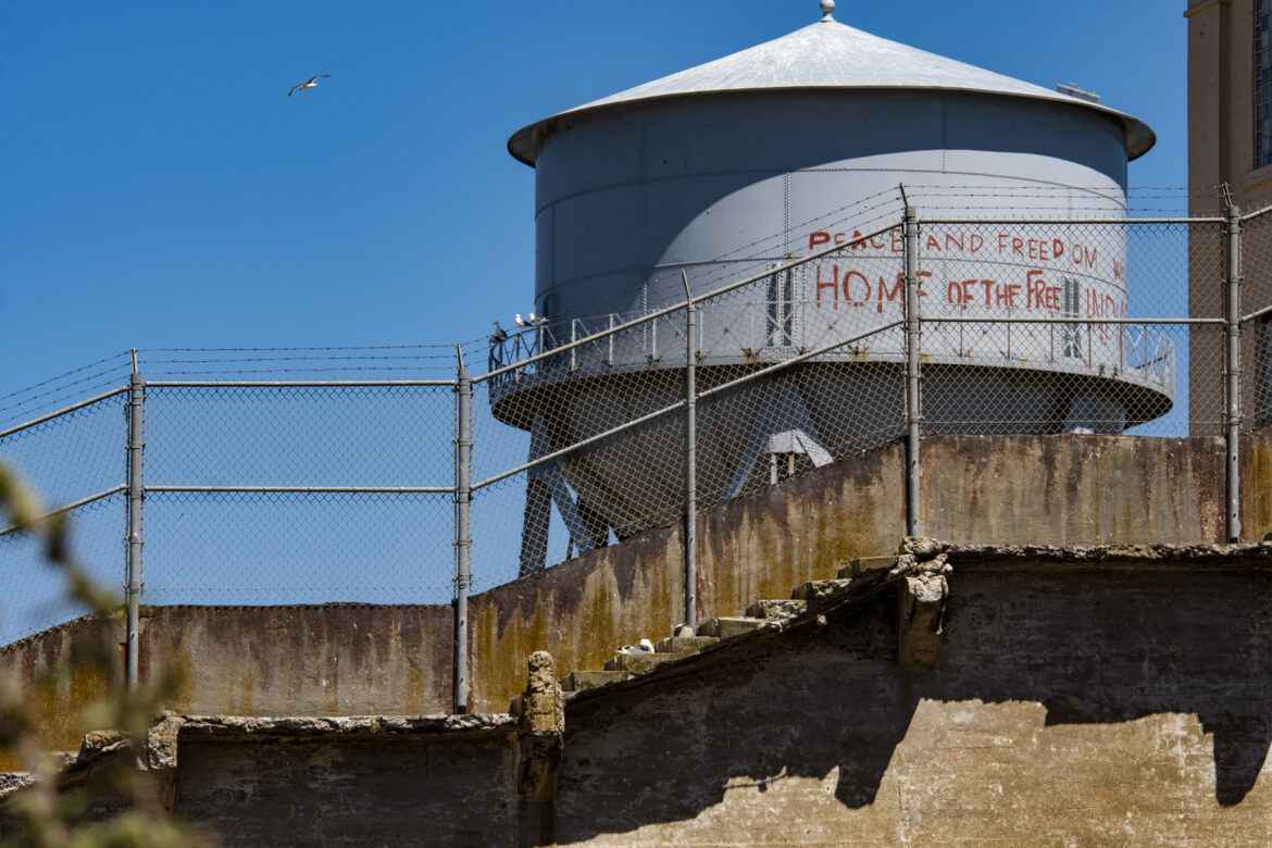 Red paint on a water tower reads: “Peace and Freedom. Home of the Free. Welcome to Indian Land.”