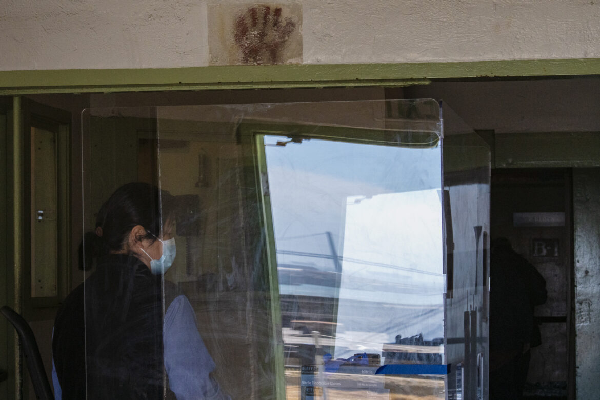 A parks conservancy employee offers information to guests from behind a plastic shield.