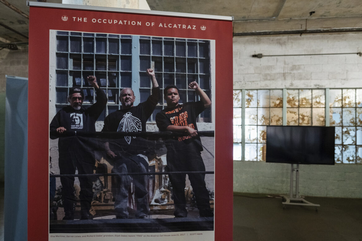 A portrait of former occupiers Eloy Martinez and Darren Laiwa with the grandson of Richard Oakes, who was a leader in the occupation, raising their fists after they repainted the word “FREE” on the shield at Eagle Plaza.