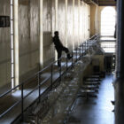 A prison guard stands inside a hall at San Quentin State Prison, his leg up on a railing fortified with razor wire, overlooking the ground floor.