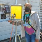 Volunteer Tiffany Williams displays an open box filled with electrical air monitoring equipment.