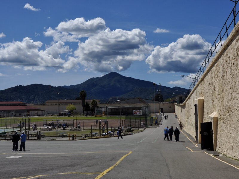 Several men gather just outside a building at San Quentin prison, with Mt. Tamalpais framed by dramatic clouds in the background. Four prisoners a tSan Quentin have tested positive for COVID-19 and their housing unit is under quarantine.