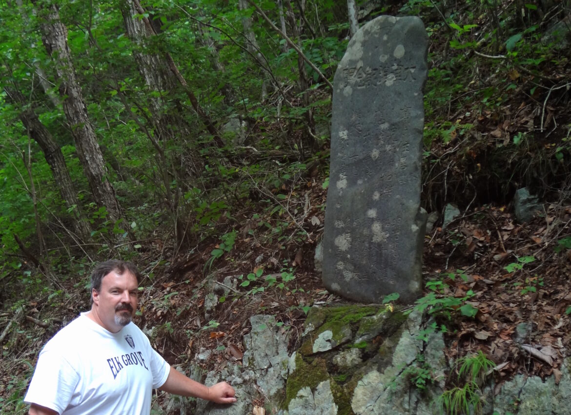 Rick Wilson stands in front of a 1930s-era “tsunami stone” in Aneyoshi Bay, Japan, that warns residents not to live below its elevation at 150 feet in August 2011. The tsunami that hit Japan that year flooded areas of up to 130 feet in elevation. Because they heeded the warning of the stone, the people in this community were safe, Wilson said.