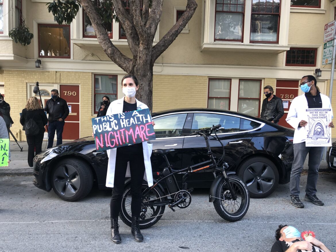 Two doctors protest outside Mayor London Breed's house on April 30, 2020, calling for more hotel rooms to be opened for people experiencing homelessness to safely shelter during COVID-19. The one in front holds a sign reading "this is a public health nightmare."
