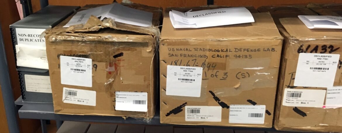 A row of cardboard boxes on a shelf labeled U.S. Naval Radiological Lab and with stickers saying "declassified"