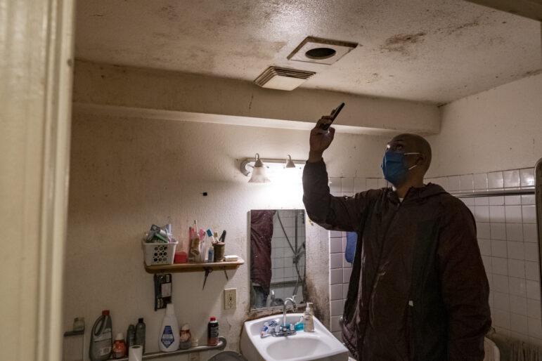 A man snaps a cellphone photo of a moldy bathroom ceiling.