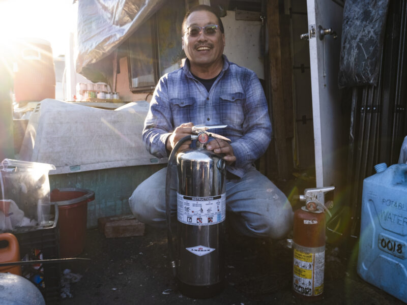 A man in a plaid shirt holds a fire extinguisher.