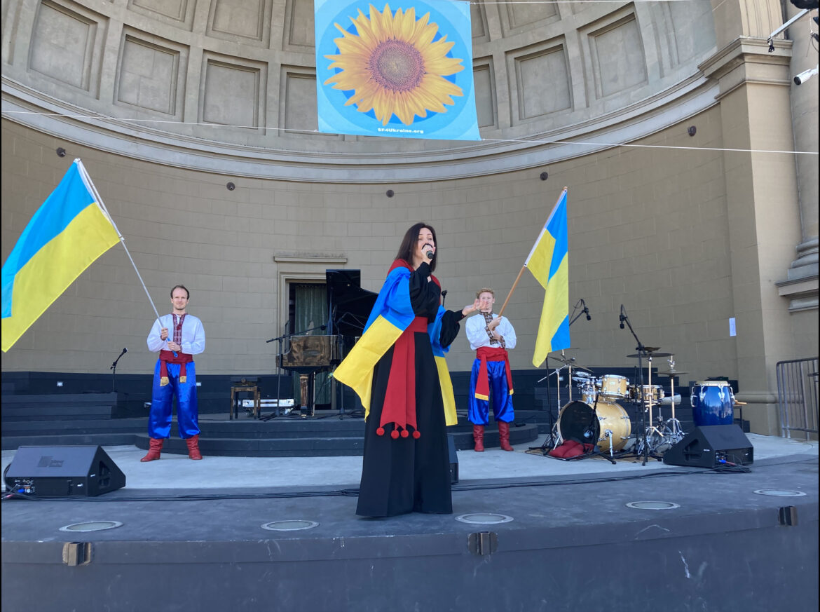 Singer at benefit concert with Ukrainian flags.