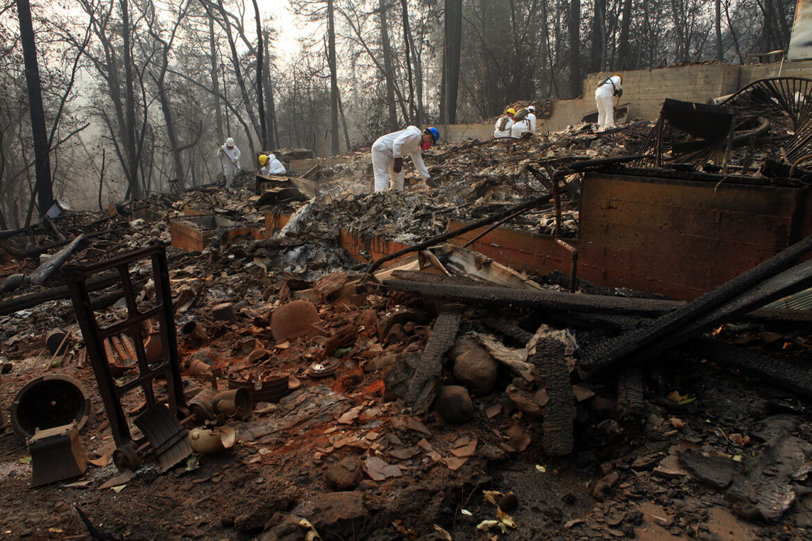 Workers in white suits sift through burned debris after the Camp Fire, the largest in California history.