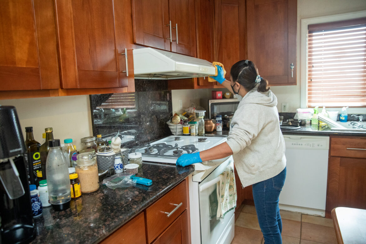 A woman facing away from the camera cleans a stovetop and range.