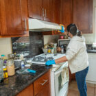A woman facing away from the camera cleans a stovetop and range.