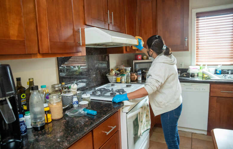 A woman facing away from the camera cleans a stovetop and range.