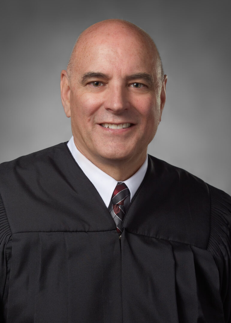 A bald white man in judicial robes is pictured.