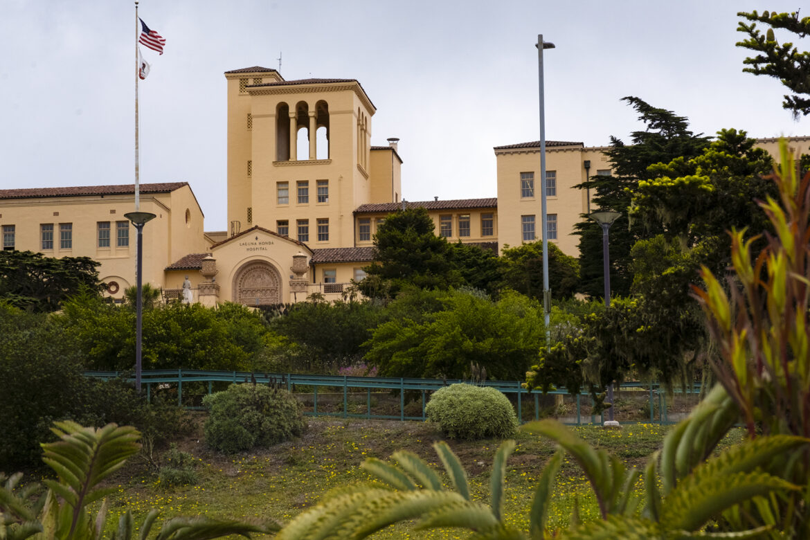 A view from a lower point on the hillside looking across lush green gardens and up toward Laguna Honda Hospital's Spanish Revival-style buildings.
