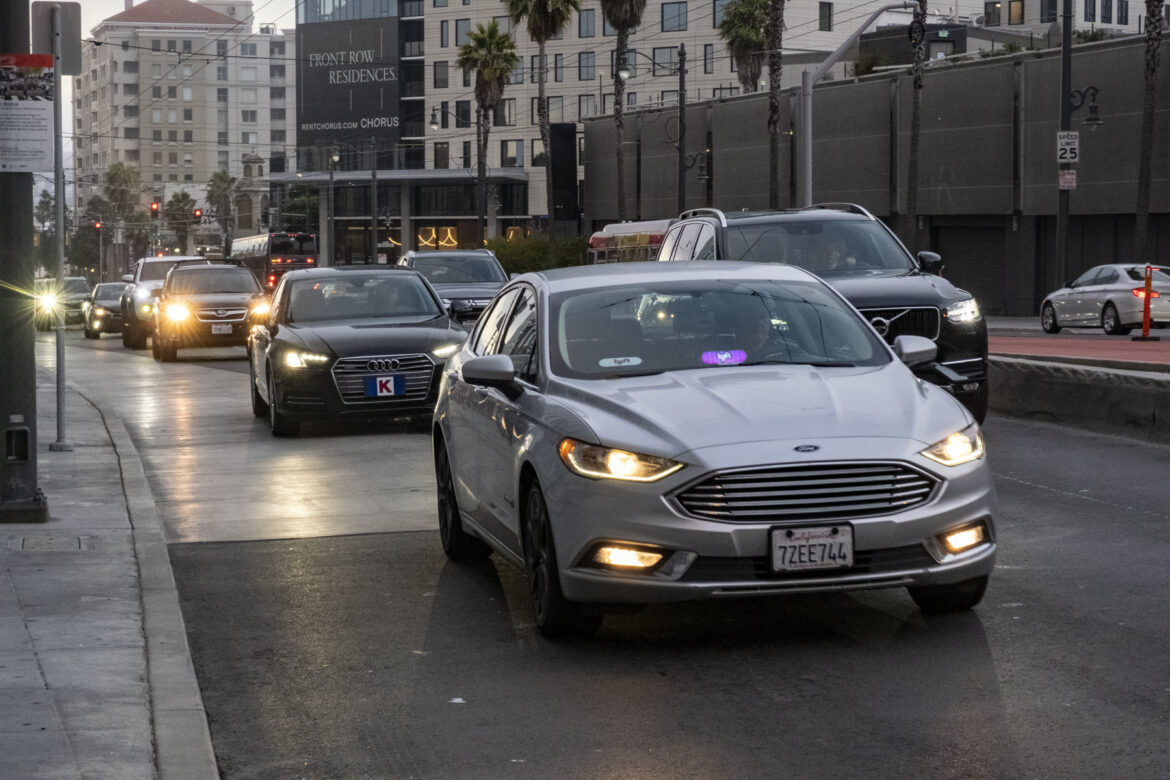 A car with a Lyft sign drives along a city street.