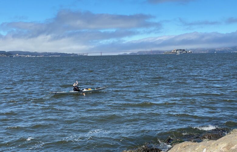 A kayaker paddles past Treasure Island as fog rolls in over the Presidio and Marin Headlands and across the Golden Gate Bridge into the San Francisco Bay.
