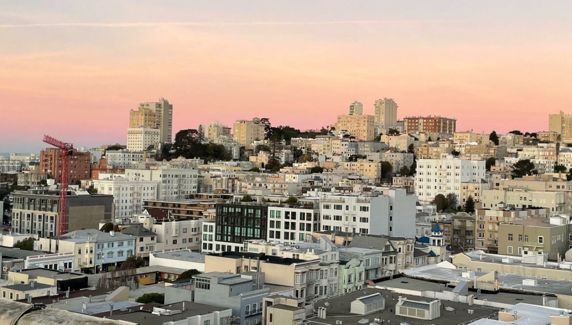 Dozens of buildings on Russian Hill are clustered together under a pink and orange sky.