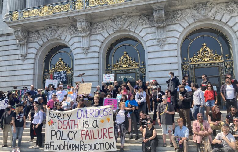A rally at City Hall with a sign reading "Every Overdose Death Is a Policy Failure" #fundharmreduction