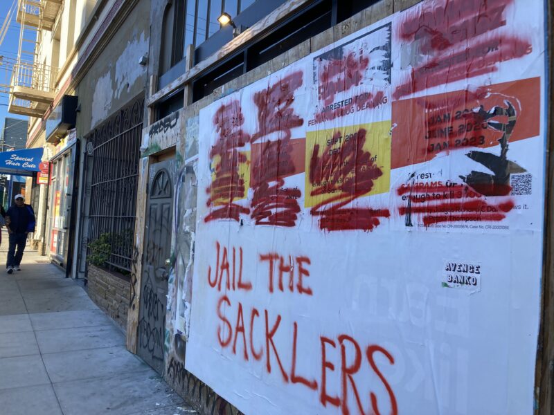 Graffiti covers a poster with the words "Jail the Sacklers"
