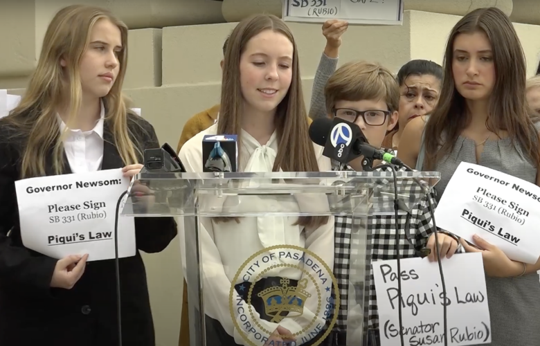 At a news conference about the passage of Piqui's Law, three teenage girls and a middle school-aged boy stand behind a clear lectern holding microphones from news outlets and bearing the seal of the city of Pasadena. They and others in the crowd hold signs, some of which read "Governor Newsom: Please sign SB 331 (Rubio) Piqui's Law" and "Pass Piqui's Law (Senator Susan Rubio)." They are referring to a bill that was introduced by California State Sen. Susan Rubio.