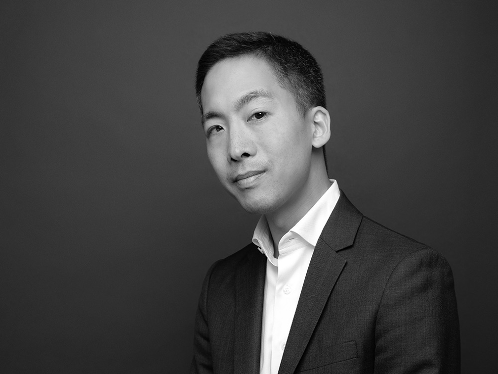Black and white portrait of an Asian man with short dark hair wearing a white button-down shirt and a suit.