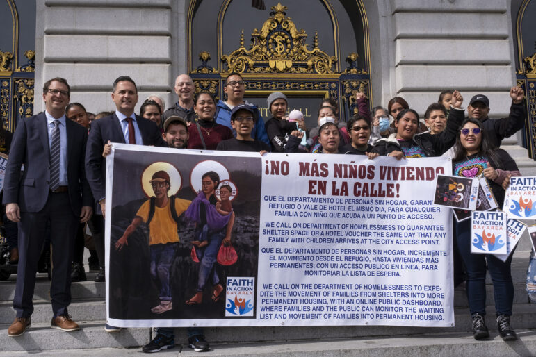 A group holds a large sign at a political event outside San Francisco City Hall.
