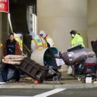 A woman walks away from a homeless encampment as city workers clear or “sweep” it, removing it from the streets in San Francisco.