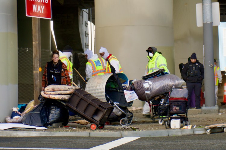 A woman walks away from a homeless encampment as city workers clear or “sweep” it, removing it from the streets in San Francisco.