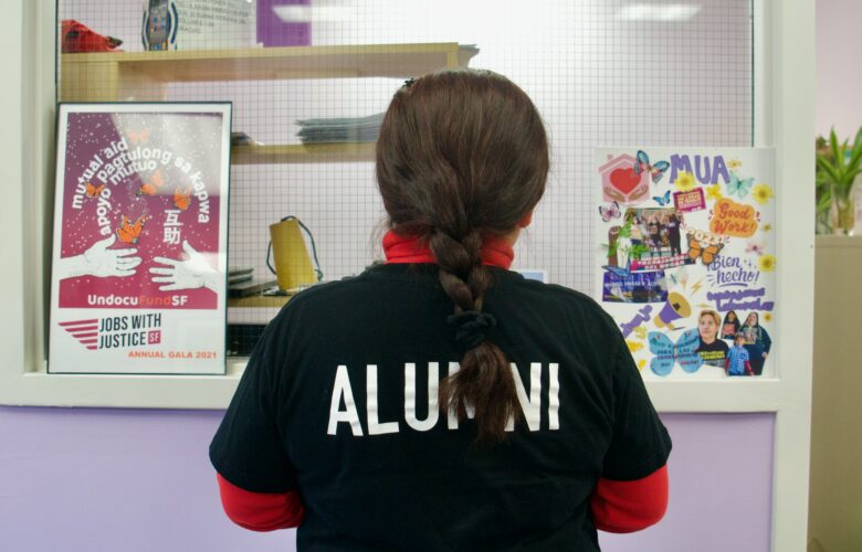 A woman in a black shirt stands with her back towards the camera. On either side of her, there are colorful posters.