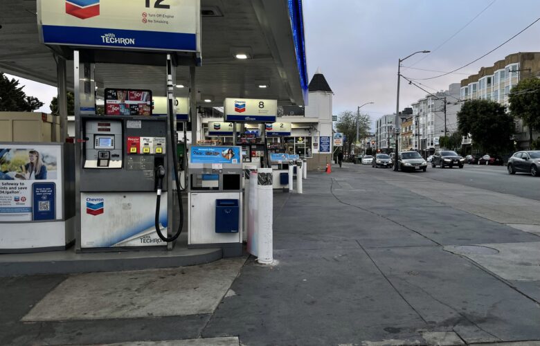A series of gas station pumps stand unused in the foreground of a dark, dusky sky.