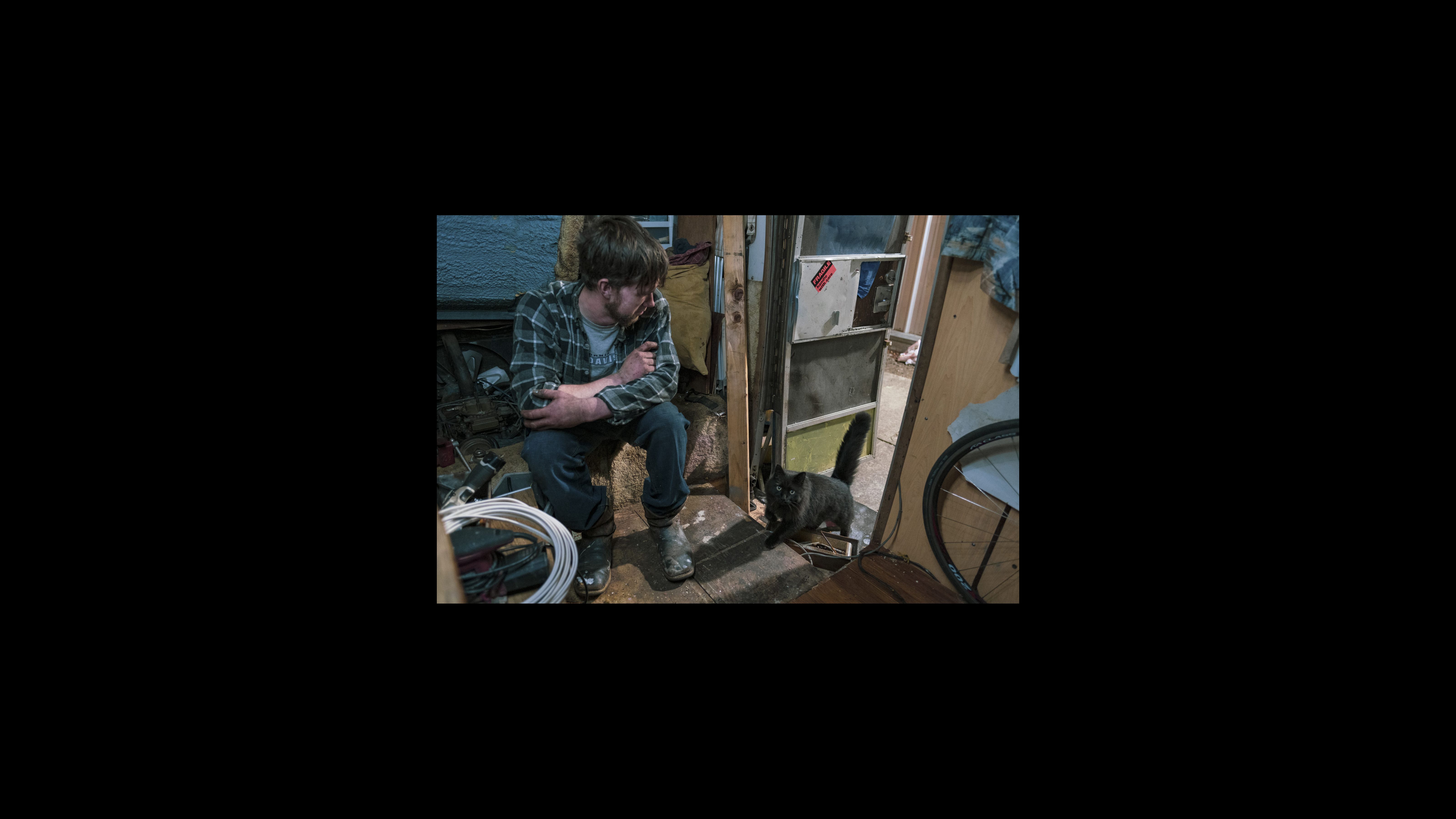 Ryan Maddry se sienta en su vehículo recreativo esperando que su gato, llamado Dog, entre antes de acostarse a fines de Febrero. Después de vivir en una tienda de campaña durante meses en el campamento de la comunidad Here / There (La Comunidad Ni Aquí / Ni Alla), compró un vehículo recreativo como un paso hacia una vivienda estable. Llamó a su vehículo "Ole Gal." Ryan Maddry se sienta en su vehículo recreativo esperando que su gato, llamado Dog, entre antes de acostarse a fines de Febrero. Después de vivir en una tienda de campaña durante meses en el campamento de la comunidad Here / There (La Comunidad Ni Aquí / Ni Alla), compró un vehículo recreativo como un paso hacia una vivienda estable. Llamó a su vehículo "Ole Gal."