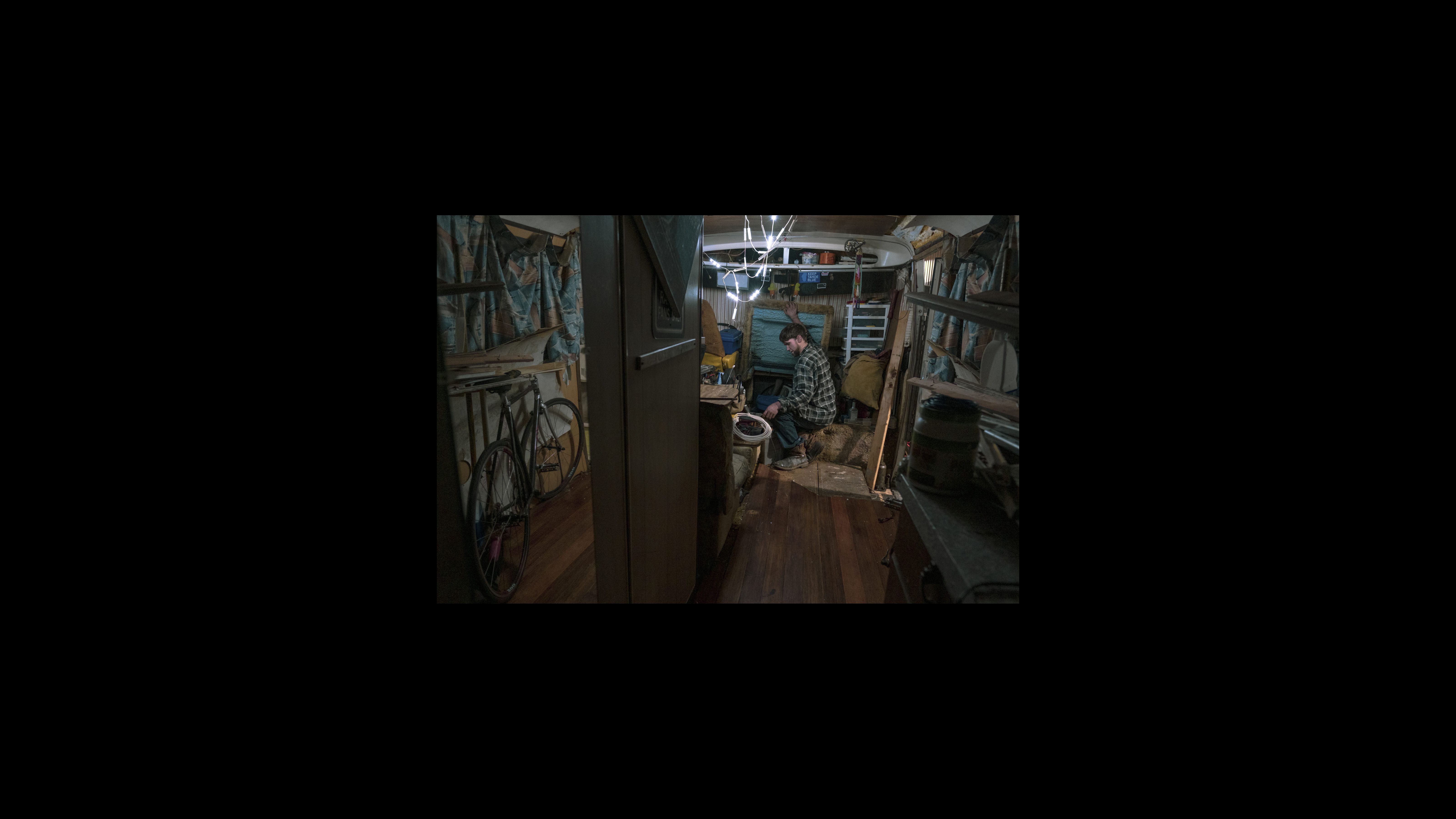 Before going to bed, Ryan Maddry pops open the doghouse engine cover in his RV, leaving a door ajar for his black cat to return home while he sleeps. Maddry works as a day laborer doing construction jobs in the Berkeley hills. In the evenings, he spends time repairing his RV, which needs insulation and a new ceiling. Maddry repairs the amenities inside his home as finances permit. Before going to bed, Ryan Maddry pops open the doghouse engine cover in his RV, leaving a door ajar for his black cat to return home while he sleeps. Maddry works as a day laborer doing construction jobs in the Berkeley hills. In the evenings, he spends time repairing his RV, which needs insulation and a new ceiling. Maddry repairs the amenities inside his home as finances permit.
