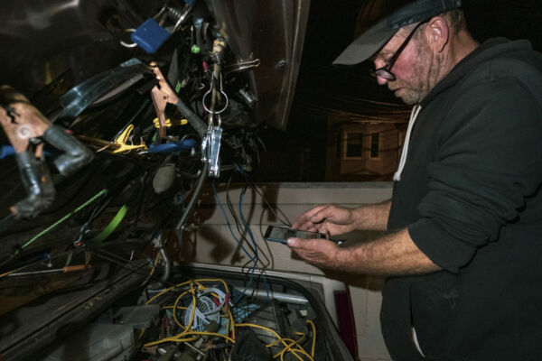 Nelson rearranges the back of his car and recharges his phone. He sleeps on four stacked blankets in the back seat. Sometimes he folds down the seat to stretch his legs into the trunk. He has attached a solar panel to the roof to power essential electronics. “The key to the solar deal is storage,” Nelson said. “I have two batteries separate from the car, so I can run a television, a DVD player and charge up my phone. Now the next question is: How long can I run it for? I would be good for an hour or two. Anything crazy and heavy like a microwave or refrigerator is going to eat you up really quick.”
But bad wiring inside his trunk has proven hazardous. One afternoon while Nelson was charging his devices, an electrical short melted the plastic of the cigarette lighter plug and filled his car with smoke. “I’m lucky I didn’t kill myself,” he said. Nelson rearranges the back of his car and recharges his phone. He sleeps on four stacked blankets in the back seat. Sometimes he folds down the seat to stretch his legs into the trunk. He has attached a solar panel to the roof to power essential electronics. “The key to the solar deal is storage,” Nelson said. “I have two batteries separate from the car, so I can run a television, a DVD player and charge up my phone. Now the next question is: How long can I run it for? I would be good for an hour or two. Anything crazy and heavy like a microwave or refrigerator is going to eat you up really quick.” But bad wiring inside his trunk has proven hazardous. One afternoon while Nelson was charging his devices, an electrical short melted the plastic of the cigarette lighter plug and filled his car with smoke. “I’m lucky I didn’t kill myself,” he said.