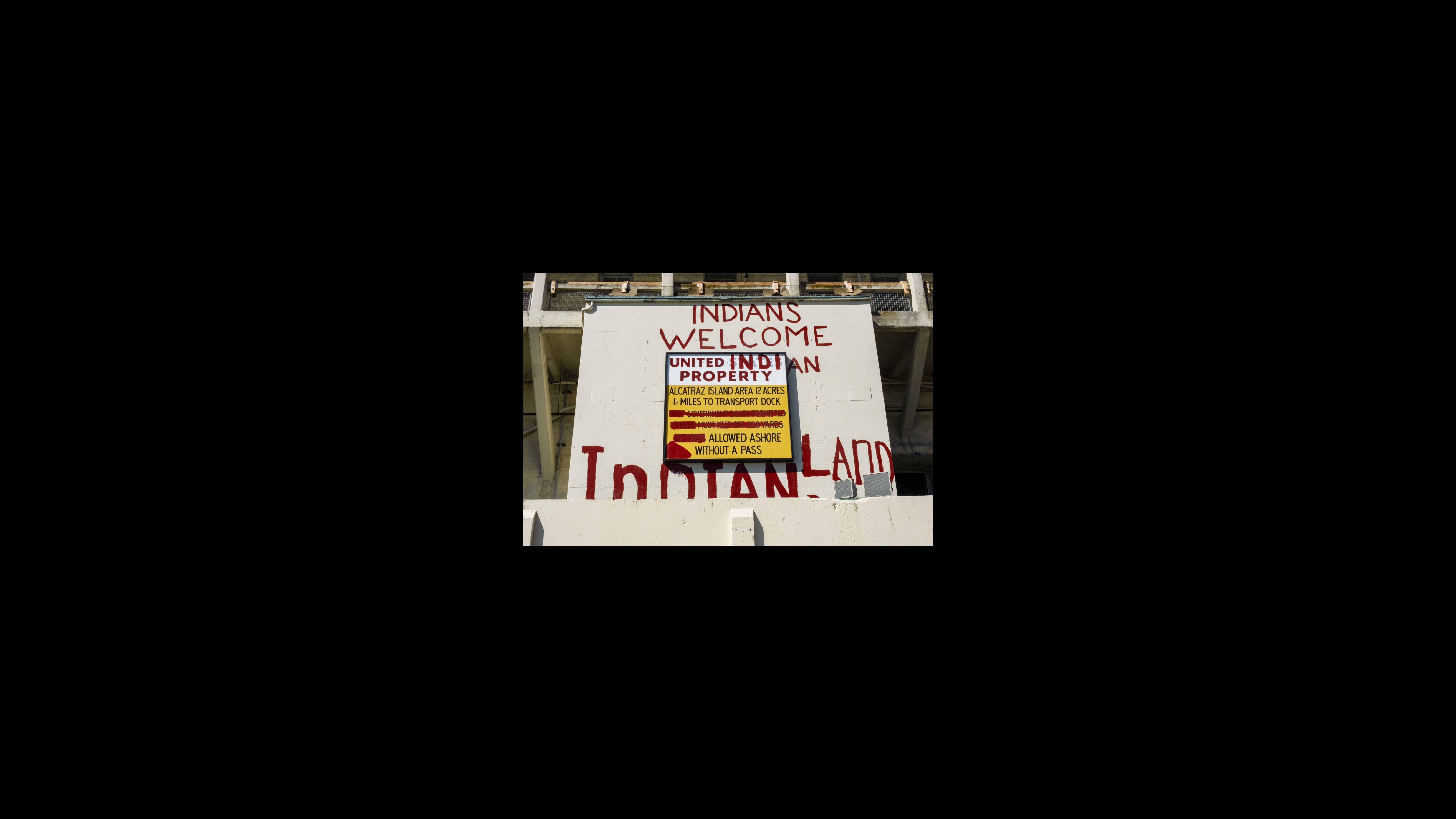 On Nov. 20, 1969, about 80 young Native American activists, including some children, sailed to Alcatraz. Members of the group occupied the island for 19 months. At the height of the occupation, 400 people lived on Alcatraz. The activists formed a nonprofit named Indians of All Tribes and spoke out against the federal government’s termination policy — whereby Congress ordered tribes disbanded and their land sold — and other hardships endured by Native Americans. The occupiers used red paint to repurpose a penitentiary sign with a new message: “Indians Welcome. United Indian Property. Alcatraz Island. Area 12 acres. 1 ½ miles to transport dock. Allowed ashore without a pass. Indian Land.”
“Occupying the island represented their ‘fight’ to live as free people in their own country,” occupation leader LaNada War Jack wrote in the Alcatraz Proposal, a document outlining the occupiers’ vision for the island. A former penitentiary sign is modified with red paint to display this text: “Indians Welcome. United Indian Property. Alcatraz Island. Area 12 acres. 1 ½ miles to transport dock. Allowed ashore without a pass. Indian Land.”