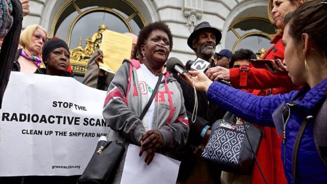Hunters Point community activist Marie Harrison, center, was a constant critic of the Navy and land developers, highlighting the radioactive and toxic contamination from the shipyard and radiation lab. She died in 2019 of a lung ailment she suspected was related to neighborhood pollution. Source: Greenaction for Health and Environmental Justice. A woman using an oxygen mask stands in front of a crowd of protesters near San Francisco City Hall, speaking to reporters