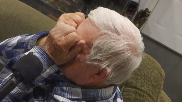 In the 1950s, the army ordered Eldridge Jones to clean up radioactive materials scientists had spread outdoors to study possible decontamination methods in the aftermath of a nuclear war. a white haired man sits on a couch crying and rubbing his eyes with his fists