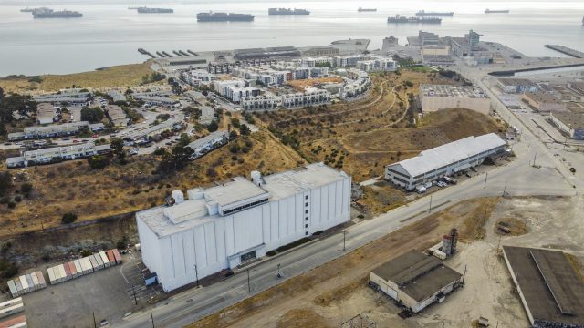 The former headquarters of the Naval Radiological Defense Laboratory, where in the years following World War II scientists oversaw exposures of hundreds of workers to radioactivity, sits just yards away from new homes at the Hunters Point Shipyard. aerial image of the six-story, nearly windowless form radiation lab building at Hunters Point in San Francisco, with housing under construction in the background