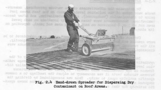 The lab used “synthetic fallout,” a radioactive mockup of the deadly poison that would cover the landscape after a nuclear attack, in numerous studies. Men equipped with minimal protective gear attempted to clean roofs and mustering grounds at Camp Stoneman in Contra Costa County in 1956. Source: Naval Radiological Defense Laboratory. A man in overalls and wearing a gas mask pushes a mechanical spreader on a rooftop in a black-and-white photo